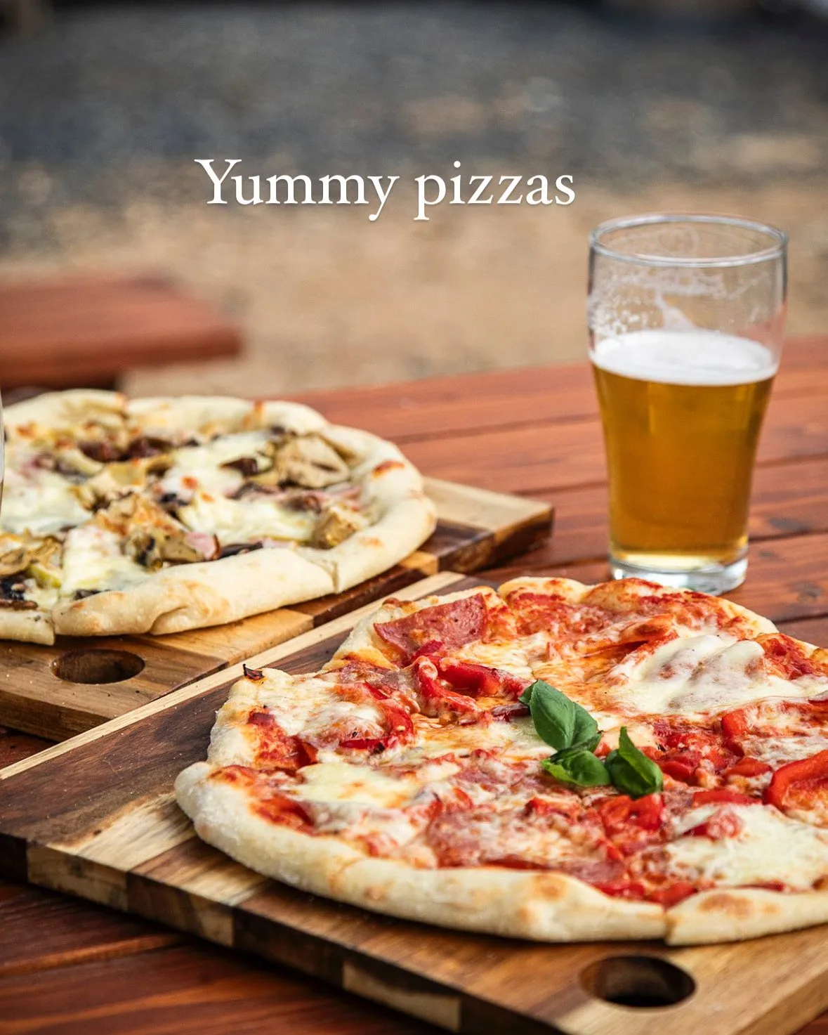 Two pizzas on wooden boards with a glass of beer
