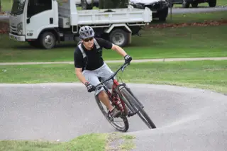 Man in black shirt and grey shorts riding a red bike on a path